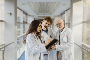 Eine Ärztin diskutiert mit einem männlichen Kollegen auf dem Flur eines Krankenhauses über ein digitales Tablet - MASF36163