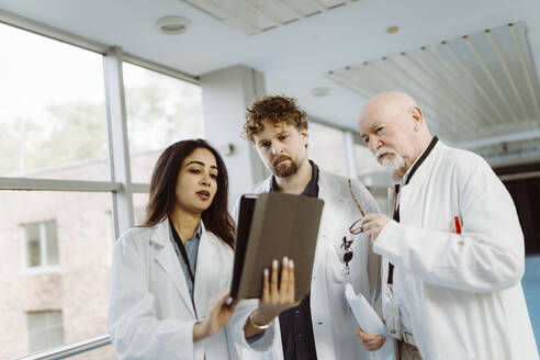 Ärztin diskutiert mit männlichen Kollegen auf dem Krankenhausflur über ein digitales Tablet - MASF36164