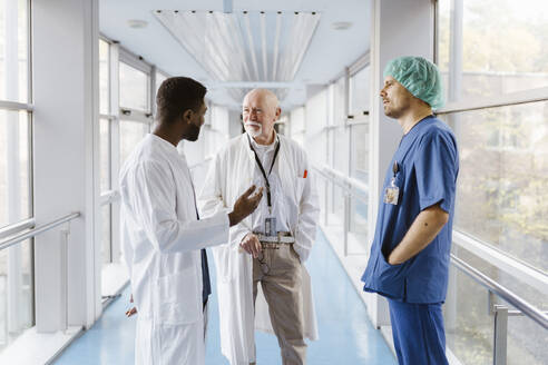 Doctors and physician discussing while standing in corridor at hospital - MASF36175