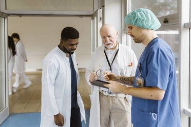 Arzt und Ärzte diskutieren über ein digitales Tablet, während sie im Krankenhaus auf dem Flur stehen - MASF36176