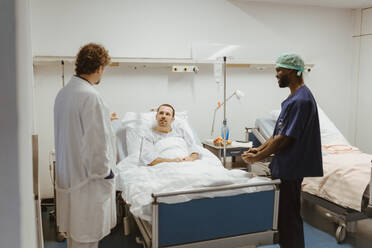 Männlicher Patient schaut den Arzt an, der neben der Krankenschwester im Krankenhaus steht - MASF36206