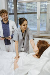 Lächelnde Krankenschwester im Gespräch mit einer älteren Patientin, die auf dem Bett eines Arztes im Krankenhaus liegt - MASF36210