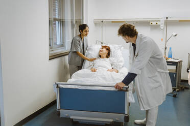 Lächelnde ältere Patientin auf dem Bett liegend, inmitten von Pflegepersonal im Krankenhaus - MASF36212