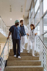 Niedriger Blickwinkel auf eine leitende Ärztin, die sich mit Kollegen unterhält, während sie eine Treppe im Krankenhaus hinuntergeht - MASF36216