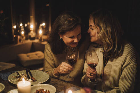 Ältere Freundinnen unterhalten sich und halten Weingläser während einer Dinnerparty bei Kerzenschein - MASF36225