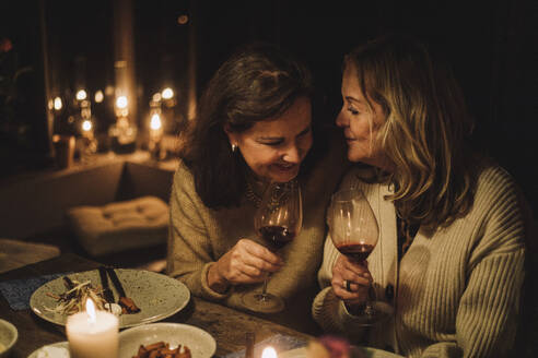 Senior female friends talking and holding wineglasses during candlelight dinner party - MASF36225