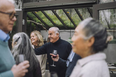 Glücklicher reifer Mann genießt mit älteren männlichen und weiblichen Freunden während einer Dinnerparty im Hinterhof - MASF36242