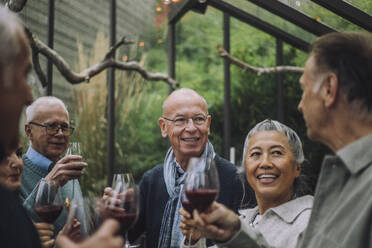 Smiling senior man talking to retired male and female friends at party - MASF36253