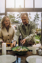 Älterer Mann bereitet den Esstisch mit einer Freundin während einer Party vor - MASF36265