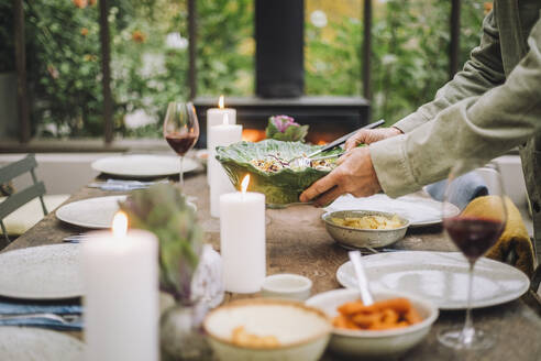 Hände eines älteren Mannes, der eine Salatschüssel hält, während er den Abendbrottisch für eine Party vorbereitet - MASF36268