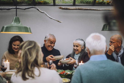 Happy male and female friends passing food bowls during dinner party - MASF36273