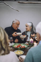 Männliche und weibliche Freunde halten Essensschalen, während sie sich auf einer Dinnerparty unterhalten - MASF36274
