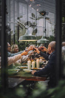 Männliche und weibliche Freunde stoßen mit Getränken während einer Dinnerparty im Hinterhof an - MASF36276