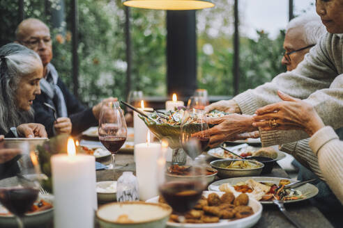 Ältere Frau serviert Salat für männliche und weibliche Freunde während einer Party - MASF36281