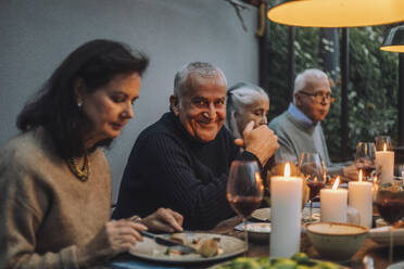 Porträt eines lächelnden reifen Mannes mit älteren Freunden während einer Dinnerparty - MASF36291