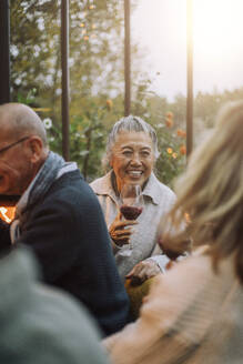 Glückliche ältere Frau hält ein Weinglas bei einer Dinnerparty - MASF36296
