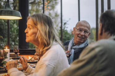 Lächelnder Mann im Ruhestand im Gespräch mit einem männlichen Freund bei einer Dinnerparty - MASF36298