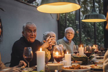 Reifer Mann mit verschränkten Händen, der mit männlichen und weiblichen Freunden auf einer Dinnerparty sitzt - MASF36299