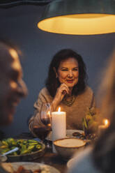 Smiling senior woman with hand on chin at illuminated dinner party - MASF36303