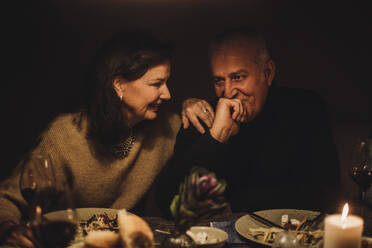 Lächelnde ältere Frau im Gespräch mit reifem Mann mit Hand am Kinn auf einer Dinnerparty - MASF36315