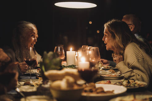 Ältere Frau im Gespräch mit einer Freundin am Esstisch während eines Abendessens bei Kerzenschein - MASF36316