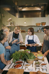 Multirassische Studenten und eine Köchin diskutieren gemeinsam während eines Kochkurses in der Küche - MASF36318
