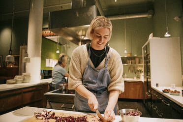 Smiling non-binary person chopping vegetables during cooking class in kitchen - MASF36320