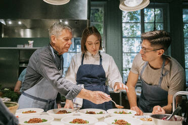 Female chef teaching male students during cooking class in kitchen - MASF36324