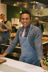 Porträt eines glücklichen reifen männlichen Studenten, der während eines Kochkurses in der Küche steht - MASF36328