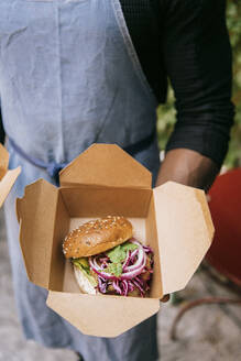 High angle view of male restaurant owner holding freshly prepared burger in box - MASF36332