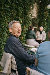 Glücklicher älterer Mann sitzt auf einem Stuhl im Restaurant - MASF36340