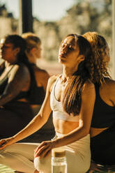 Freundinnen, die Rücken an Rücken in einem Yogakurs sitzen und üben - MASF36377