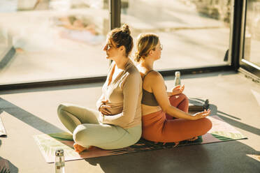 Frauen beim Üben von Atemübungen, Rücken an Rücken sitzend, während einer Yogastunde - MASF36379