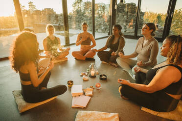 Multiracial female friends meditating together sitting cross-legged at retreat center - MASF36403