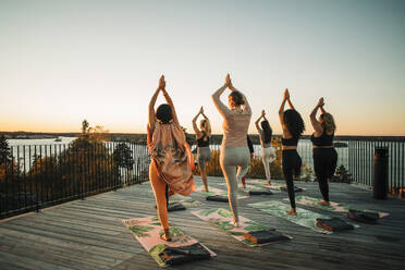 Rückansicht von Freundinnen, die Vrikshasana auf der Terrasse des Retreat-Zentrums üben - MASF36409