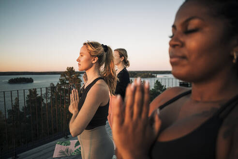 Woman with hands clasped exercising with female friends at patio - MASF36412