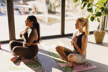 Frauen machen Atemübungen, während sie auf Übungsmatten im Rückzugszentrum sitzen - MASF36425