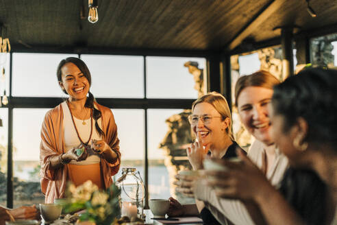 Happy woman holding crystals while talking to female friends at retreat center - MASF36480