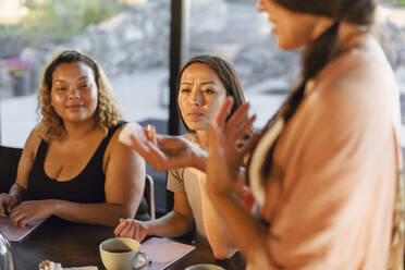 Woman explaining crystal to female friends at retreat center - MASF36482