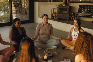 Multiracial female friends holding hands while doing meditation at retreat center - MASF36508