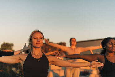 Woman with arms outstretched exercising with female friend at sunset - MASF36516