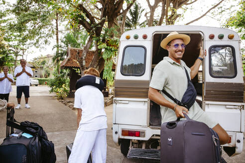 Lächelnder männlicher Tourist, der mit seinem Gepäck aus dem Van am Urlaubsort aussteigt - MASF36539