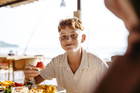 Portrait of boy having watermelon slice for breakfast in resort during vacation - MASF36554