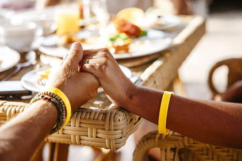Ausgeschnittenes Bild eines heterosexuellen Paares, das am Tisch in einem Ferienort Händchen hält - MASF36556