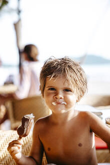 Porträt eines lächelnden Jungen, der an einem sonnigen Tag in einem Ferienort ein Eis isst - MASF36561