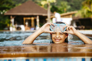 Porträt eines lächelnden Mädchens mit Schwimmbrille im Pool eines Ferienorts - MASF36568