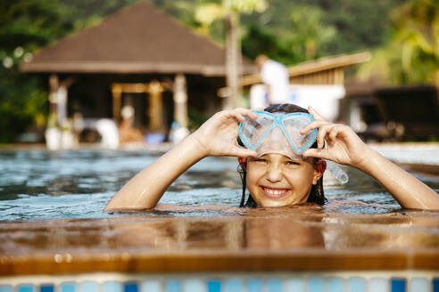 Porträt eines lächelnden Mädchens mit Schwimmbrille im Pool eines Ferienorts - MASF36568