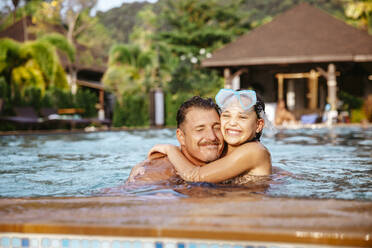 Glückliches Mädchen umarmt Vater beim Schwimmen im Pool am Urlaubsort - MASF36569