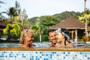 Cheerful girl enjoying with parents in swimming pool at resort during vacation - MASF36572