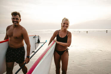 Glückliches Paar mit Paddleboards am Strand bei Sonnenuntergang - MASF36605